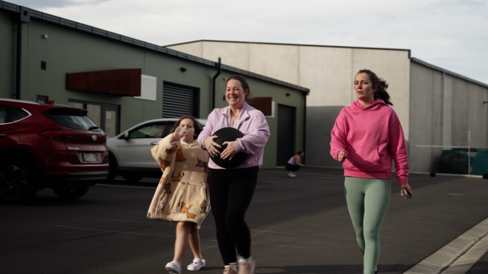 A mother and daughter laugh while carrying a medicine ball